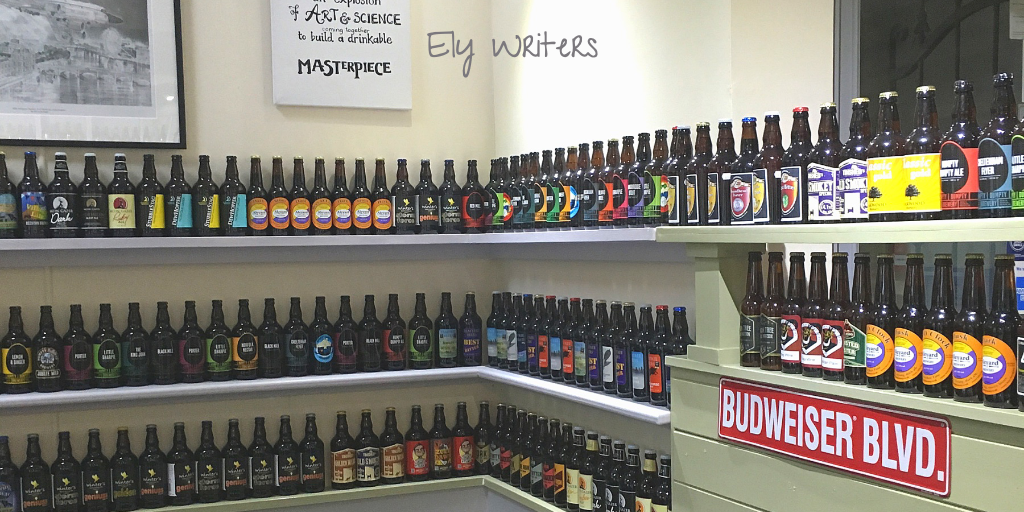 Shelves of beer bottles. A red Budweiser Boulevard street sign. A on the wall that reads "Definition of CRAFT BEER: An explosion OF ART & SCIENCE to build a drinkable MASTERPIECE". Overlaid top centre is the text "Ely Writers".