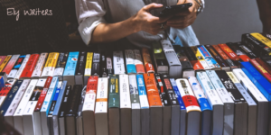 A person holding a smartphone over a selection of books arranged in two rows placed spine up.